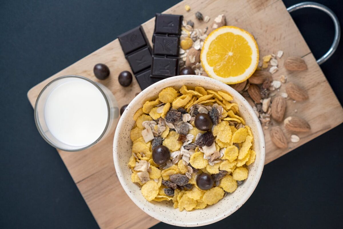 A close-up of a nutritious breakfast featuring cereal, chocolate, orange, and milk on a wooden board.