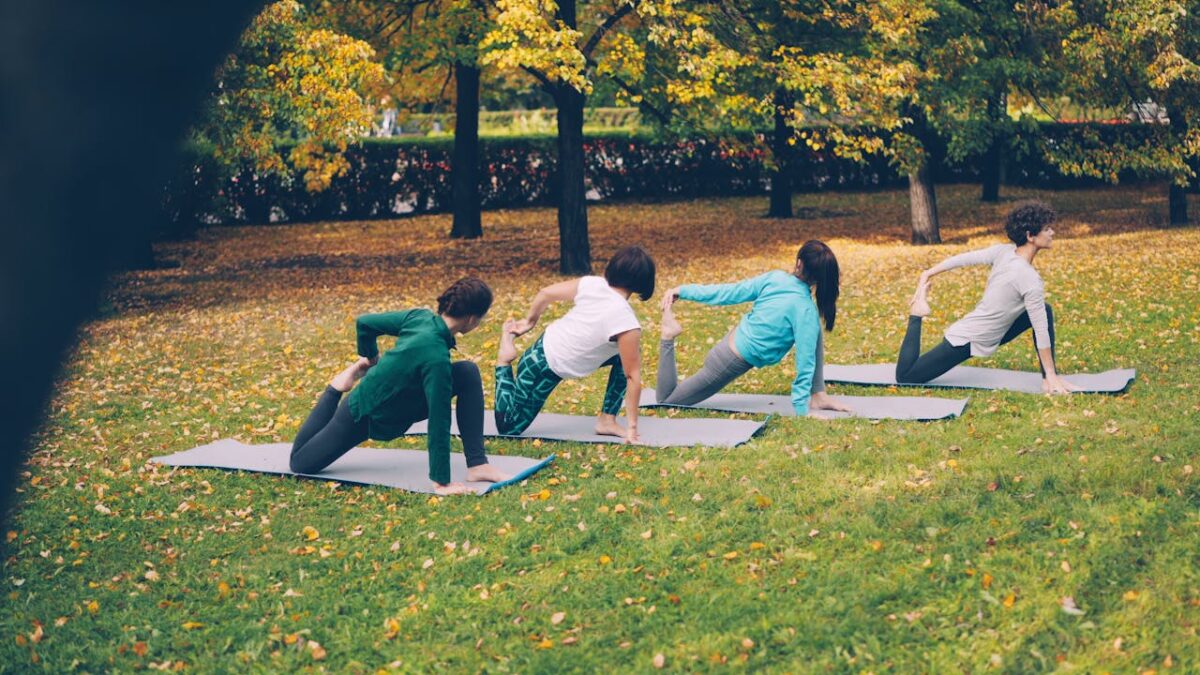 Adults practicing yoga poses on mats outdoors in a park during autumn.