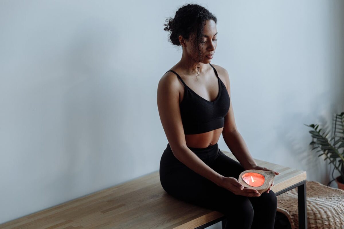 A woman in black activewear meditates with a candle, seated indoors for mindfulness and relaxation.